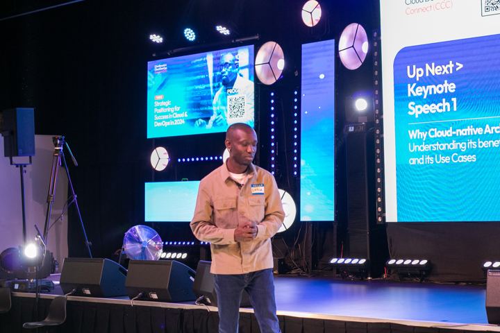 Keynote speaker on stage beside a screen reading Up Next: Keynote Speech 1