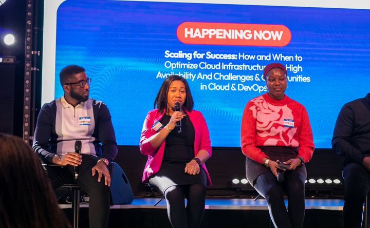 Four panellists on stage under a screen reading Happening Now: Scaling for Success